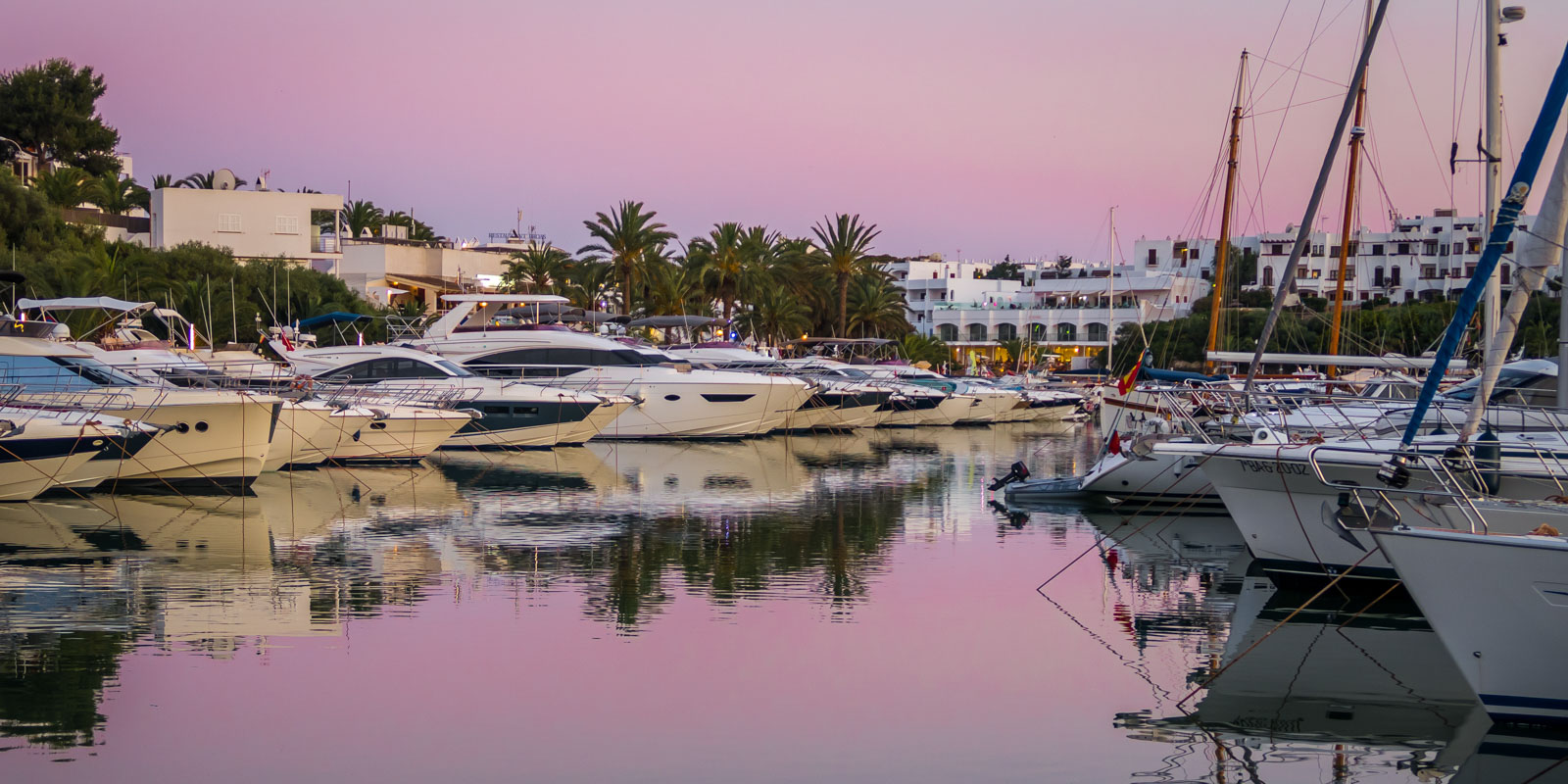Marina of Cala d’Or, Mallorca, at sunset with boats and yachts moored in the harbor.
