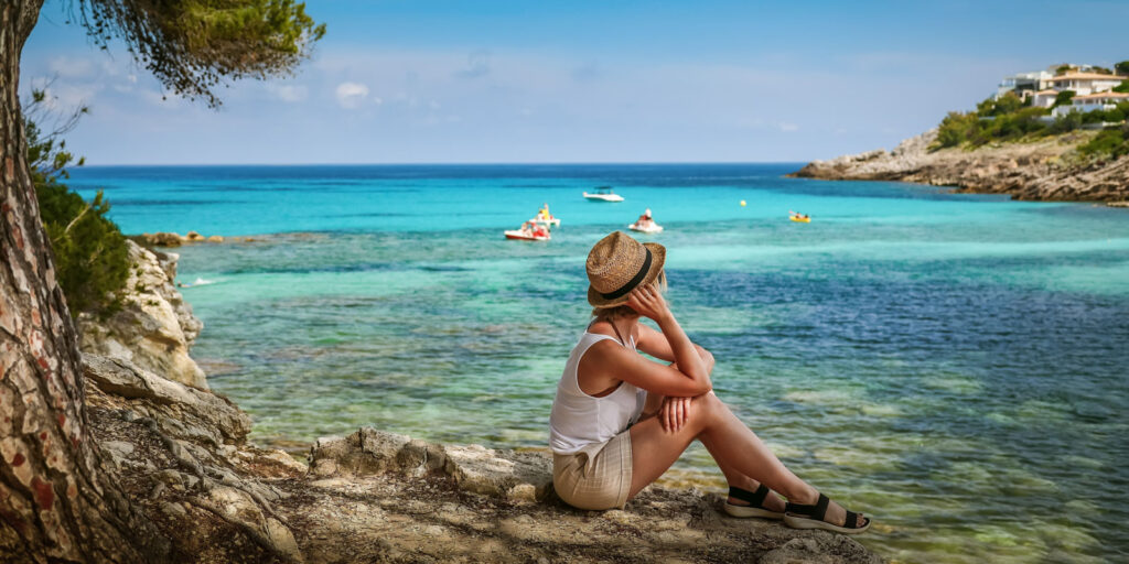 Woman sitting by the sea on a cove in Mallorca to explain if you can drink on the beach in Mallorca