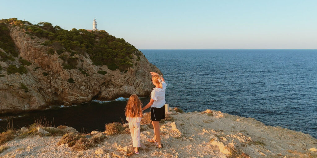 Mother and daughter enjoying a day near Cala d'Or during the sunset and with a lighthouse and the Mediterranean Sea on the background to explain where to stay in Majorca for families