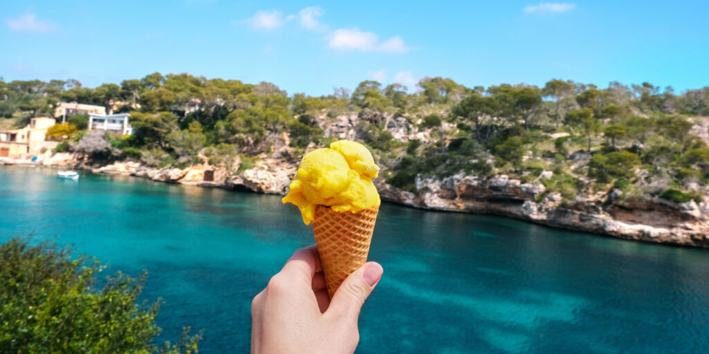 Enjoying an icecream by a cove in Mallorca to explain when is the ideal season for a beach holiday in Mallorca